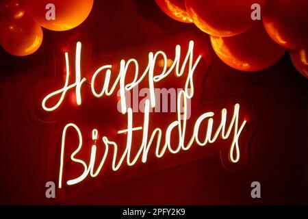 Goiania, Goias, Brazil – March 18, 2023:  Written "Happy Birthday" with neon light on a red background and with several balloons around. Stock Photo