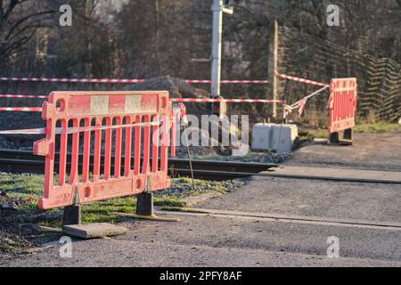 Closed railway tracks under construction or maintenance of a crossing with a road. Reflection orange-red-white barriers and a warning tape. Stock Photo