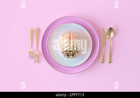 Gold human brain on a plate. Concept of abuse, destructive relationships. Human brain with plate, fork, spoon, knife. Top view, creative composition. Stock Photo
