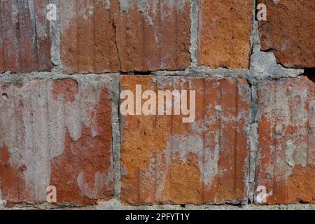 Details of an exposed, divider wall. Cracks and holes in the red wall. Cement is falling off the large red blocks. Stock Photo