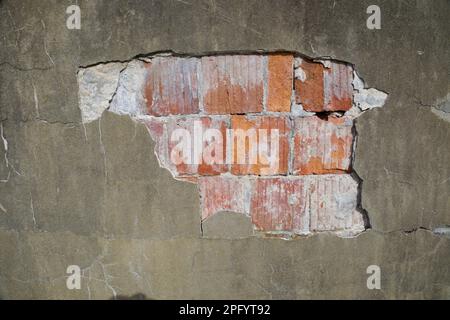 Details of an exposed, concrete divider wall falling apart, cracks and holes in the wall. Inside the wall is red brick. Stock Photo