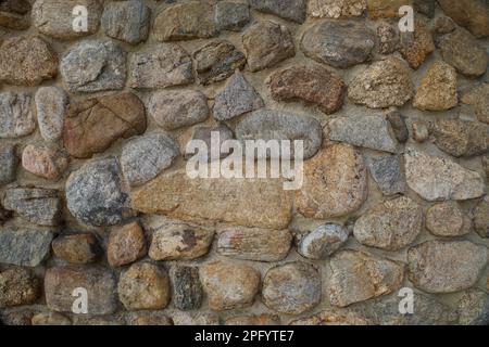 Texture of a real stone wall. Part of rock wall as a background or texture.  Different shapes, sizes, and colors combined together. Uneven surface. Stock Photo