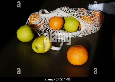 fresh green apples and oranges in cotton string bag on grey table Stock Photo