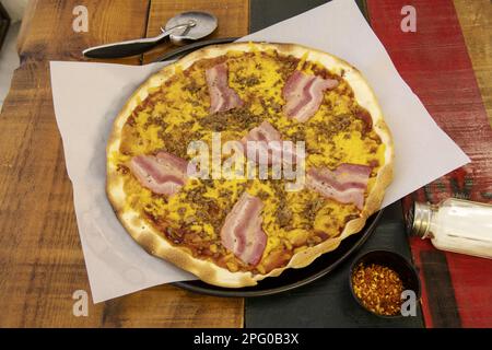 A wonderful medium thin crust pizza with bacon, various meats, cheddar cheese and pomodoro on a colorful wooden table Stock Photo