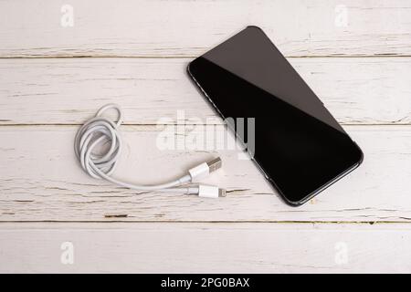 Phone with carbon fiber case and coiled white charging cable on white wooden table Stock Photo