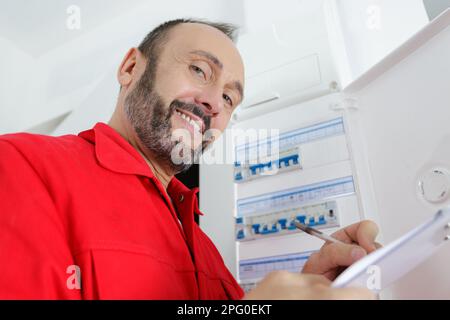 mature electrician stood by fusebox Stock Photo