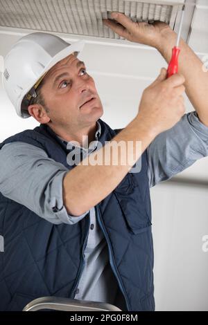 male worker fixes the lamp to the ceiling Stock Photo