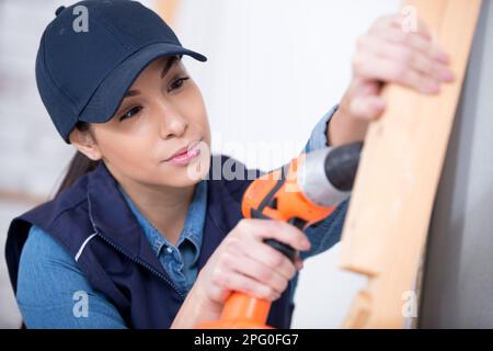 serene woman using electric screwdriver on wooden plank Stock Photo