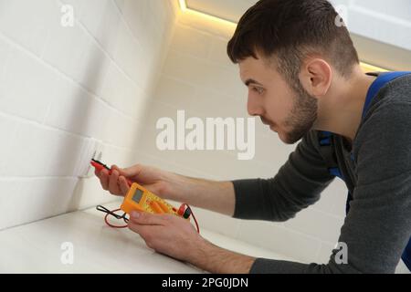 Professional electrician with tester checking voltage indoors Stock Photo