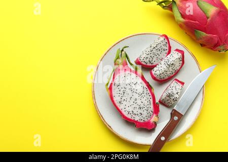 Plate with delicious cut white pitahaya fruit and knife on yellow background, flat lay. Space for text Stock Photo