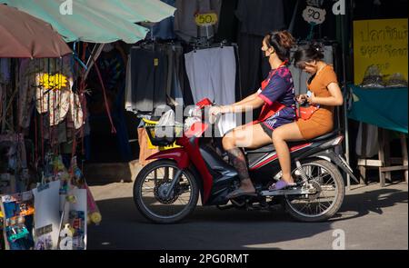 SAMUT PRAKAN, THAILAND, FEB 13 2023, Two women rides on motorcycle at the street with stalls. Stock Photo