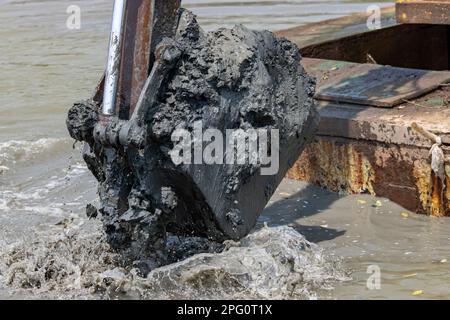 Dredging the bottom of water area, view of the bucket of the floating excavator full of mud Stock Photo