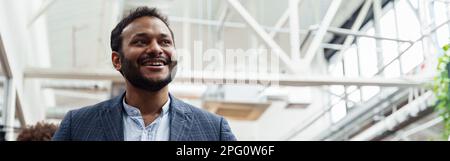 Smiling indian businessman drinking coffee and looking side while standing in office Stock Photo