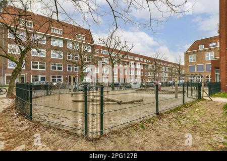 a fenced area in the middle of a residential area with cars parked on the street and buildings behind it Stock Photo