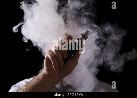 Man using electronic cigarette against black background, focus on hand Stock Photo