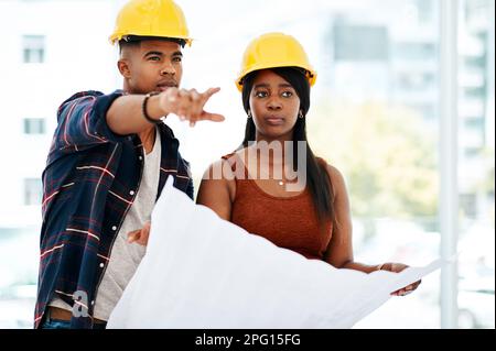 Architects see space a little differently. a young man and woman going over a blueprint in a modern office. Stock Photo