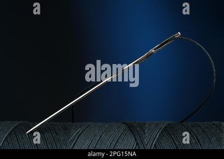 Black sewing thread with needle on dark blue background, closeup Stock Photo