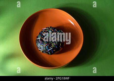 Colourful donuts in orange plate on green background. Top view Stock Photo