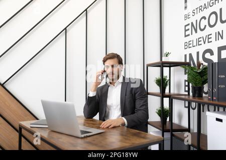 male financier sitting at table with laptop and making hot calls Stock Photo
