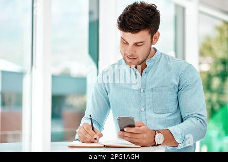 Making notes helps him improve. a handsome young businessman making notes while siting at a table in his office. Stock Photo