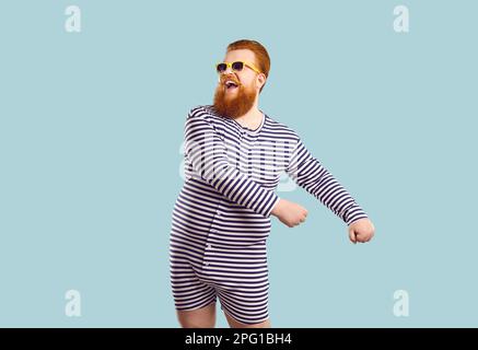 Funny bearded chubby man in sailor leotard having fun on pastel light blue background. Stock Photo