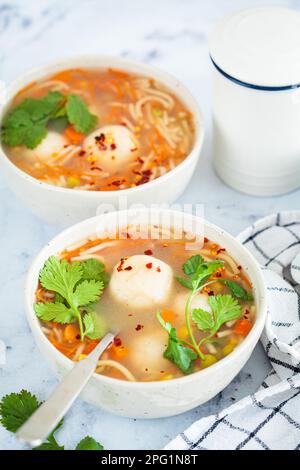 Potato balls soup with noodles and vegetables in a white bowl, white background. Vegan food concept. Stock Photo