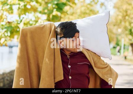 Young man in pajama is outdoors on the street. Feels sleepy Stock Photo