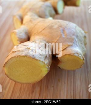 Part of an irregularly shaped fresh ginger root on a wooden cutting board Stock Photo