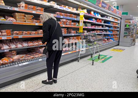 Elderly senior woman with shopping trolley cart looking at chicken meat products on Morrisons supermarket shelves store Great Britain UK  KATHY DEWITT Stock Photo