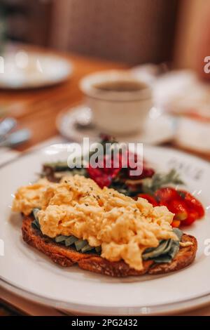 Traditional breakfast toast with scrambled eggs, pieces of avocado and cherry tomatoes on the plate Stock Photo