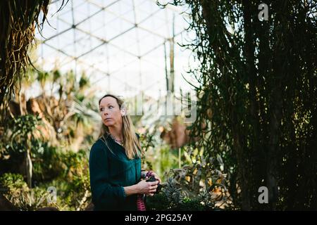 Woman with camera in dome greenhouse with plants and sunshine Stock Photo