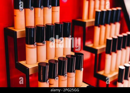 Mock up beige tubes of face foundation on a red stand in a store. The concept of decorative cosmetics for the face Stock Photo