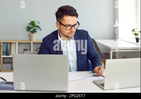Focused businessman using two laptop computers in office Stock Photo