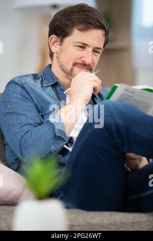 young man sitting doing a crossword puzzle looking thoughtfully Stock Photo