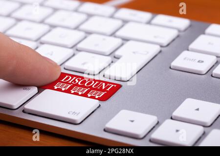 Finger pressing on discount button on red keyboard. Online sales. Three shopping carts are next to the finger and words Stock Photo