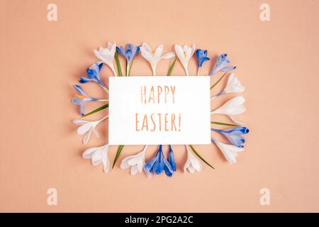 Card with words Happy Easter and frame of crocus flowers on neutral background. Top view, flat lay. Stock Photo