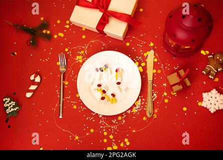 Plate with tablets, pills and capsules on bright holiday background. It served with fork and knife. Gift boxes, christmas cookies, lantern and fir bra Stock Photo