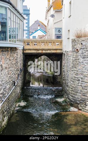 The River Lim flows through the old town of Lyme Regis in Dorset under the Buddle Bridge. Stock Photo