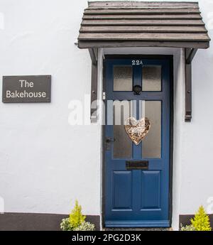 A blue painted door with glass panels, wooden porch and a heart decoration. The house name is The Bakehouse. Stock Photo