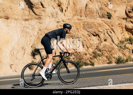 Cyclist in black sportswear doing intense training outdoors. Side view of a triathlete on a bicycle. Stock Photo