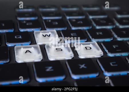 White highlighted gaming keys with blue light. Powerful dark notebook keyboard close-up. Tech, IT, e-sport, computer science background Stock Photo