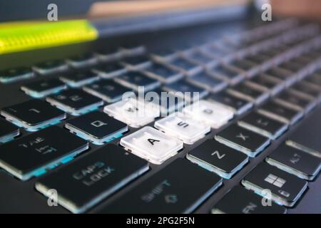 Highlighted gaming keys with blue light and focus blur. Powerful dark notebook keyboard close-up. Tech, IT, e-sport, computer science background Stock Photo