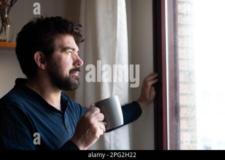 middle-aged man sipping a cup of coffee looking out the window inspired in thoughtful reflection Stock Photo