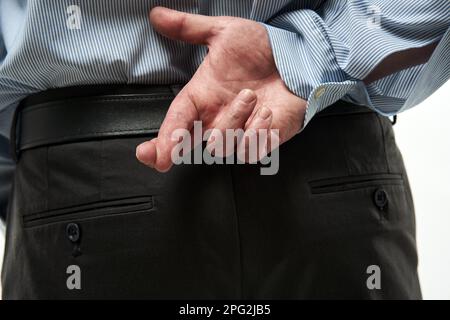Dishonest and deceitful businessman's hand with crossed fingers by his back Stock Photo