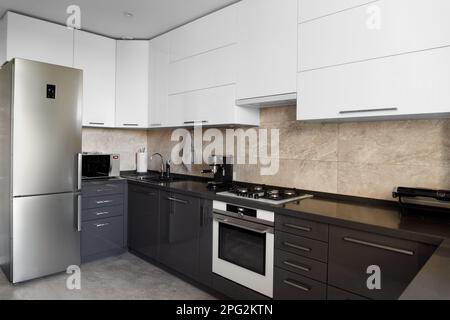 The kitchen in the apartment. The design of the kitchen room. Gray kitchen interior with white cabinets. Built-in oven in the interior of the kitchen. Stock Photo