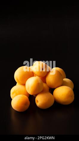 Apricots on a black background. A handful of apricots on a dark background with reflection. Useful summer fruit. Stock Photo
