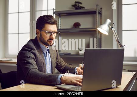 Serious businessman working on laptop in modern office Stock Photo