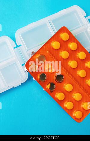 Plastic container for pills and yellow pills pack on blue background close up Stock Photo