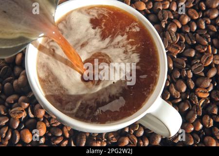 Pouring black coffee into white ceramic cup. Top view. Close up. Hot coffee drink pour into cup from shiny moka pot coffee maker. Roasted coffee beans Stock Photo