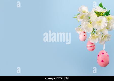 Three lovely pink Easter eggs suspended from a blooming branch against a calming blue backdrop, a perfect image of hope and joy Stock Photo
